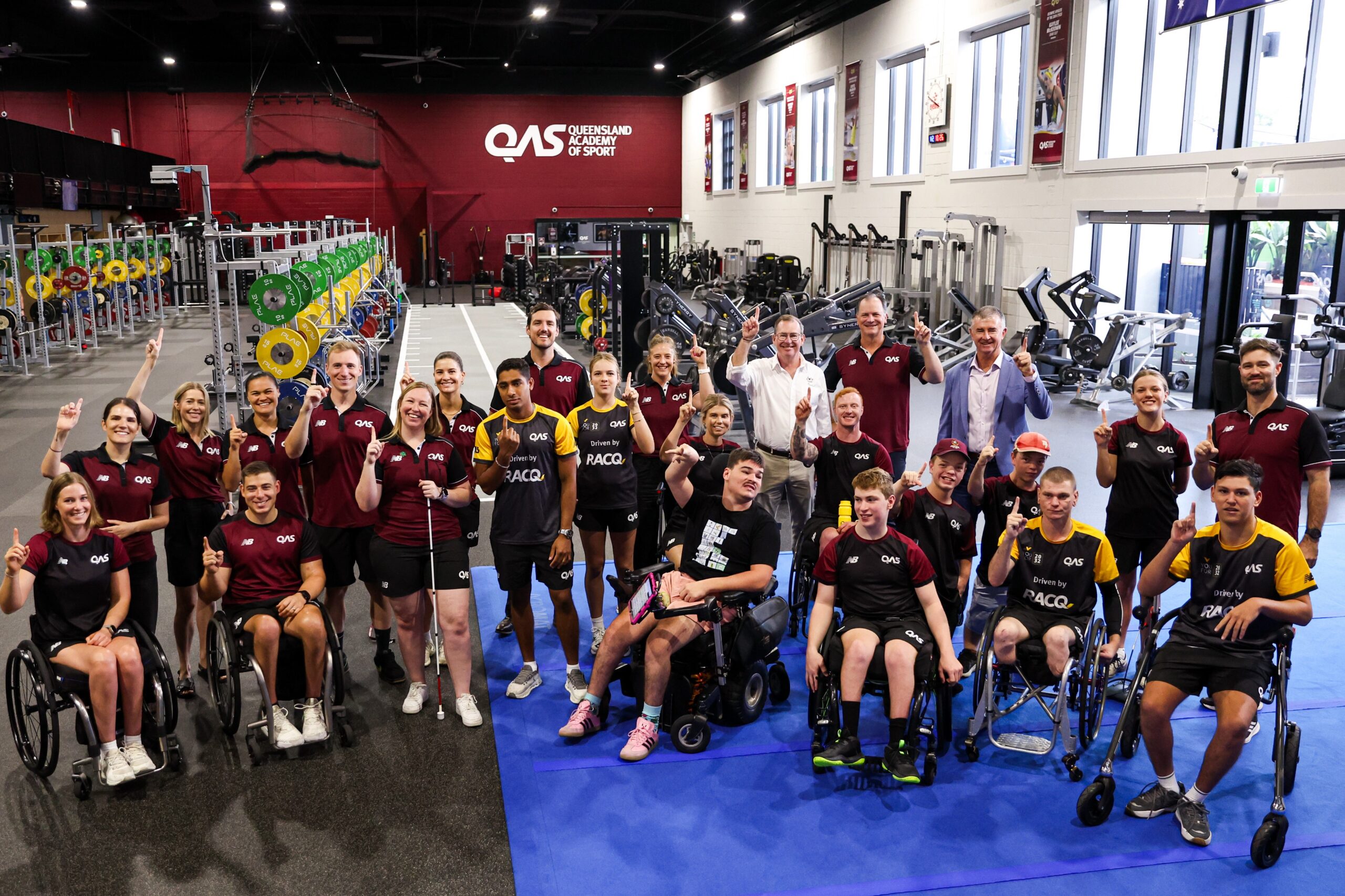 A group of athletes wearing QAS uniforms pose in the gym